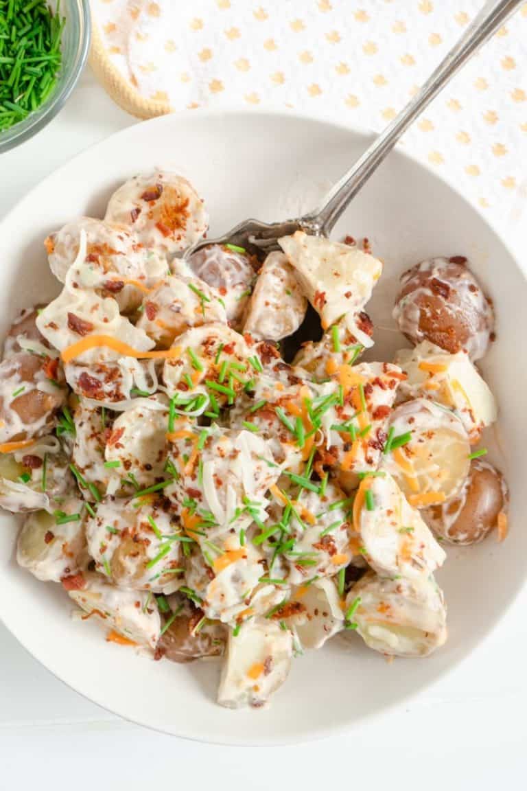 Loaded Potato salad with baby potatoes, bacon bits, cheese and green onions in a white dish.