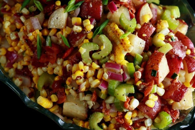 Potato Salad made with new potatoes, corn, celery, red onions, and bacon in a glass bowl.