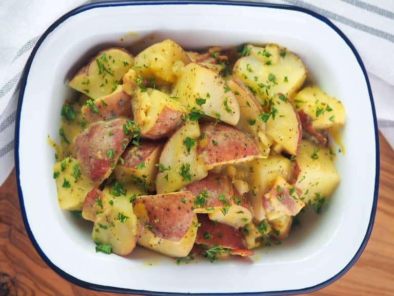 German Potato Salad topped with parsley in white serving dish.