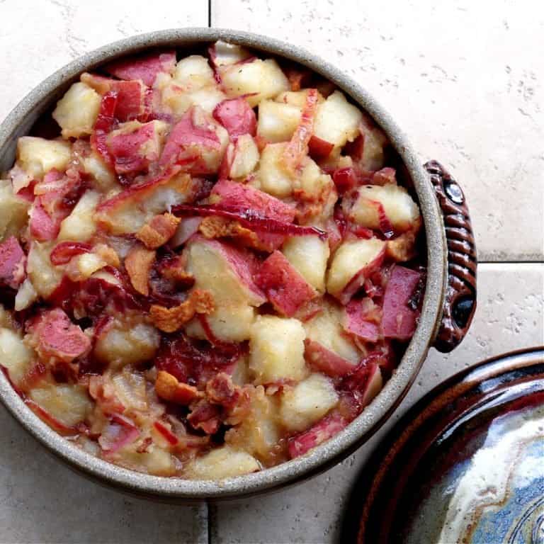 Hot German Potato Salad topped with crispy bacon in a ceramic bowl.