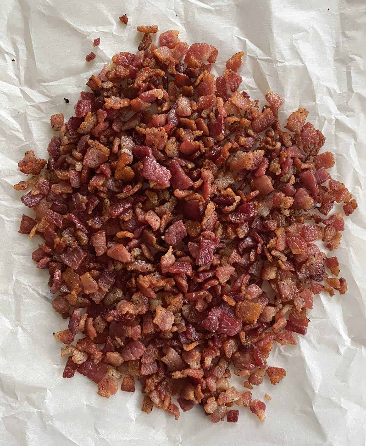 A pile of freshly cooked bacon bits on a piece of parchment paper.
