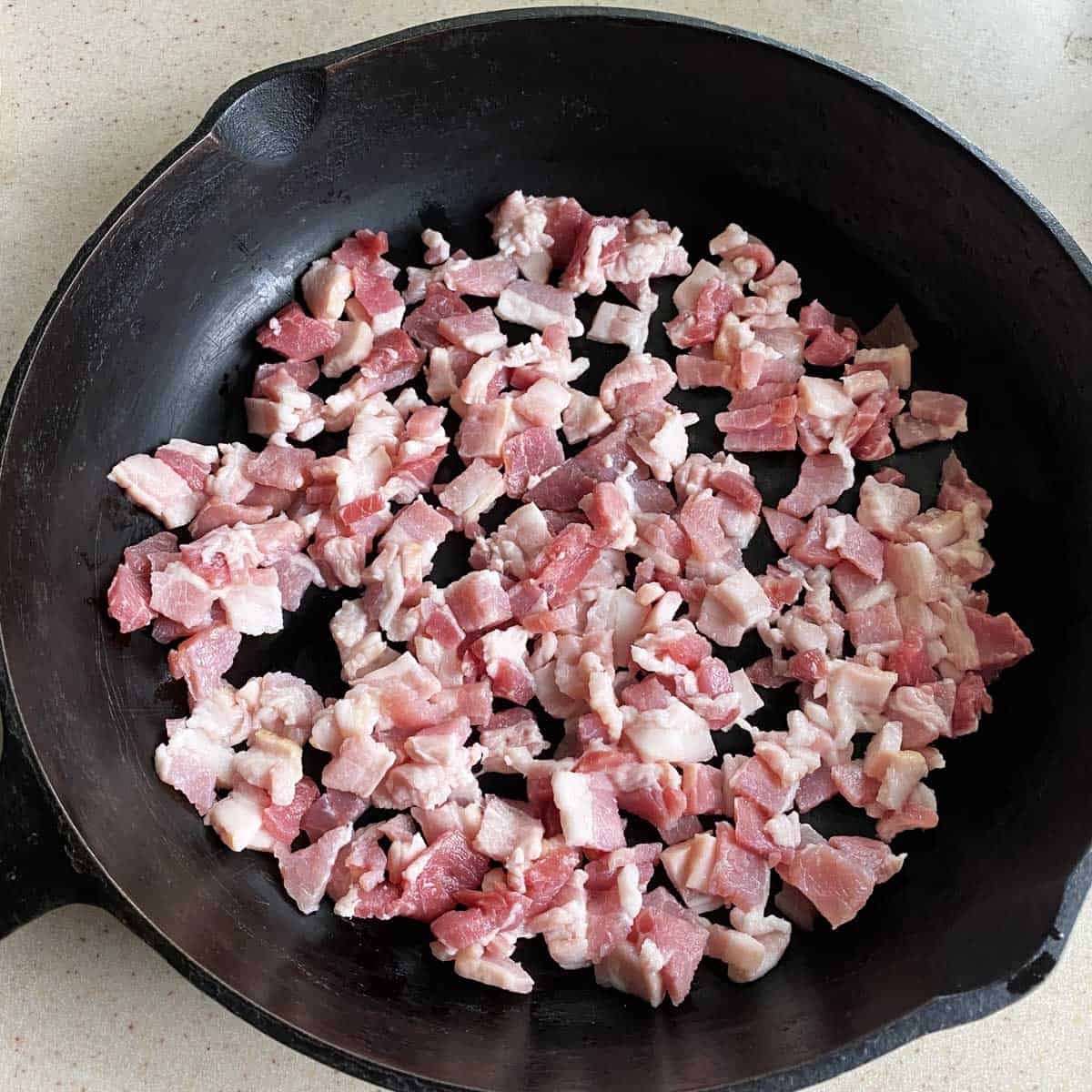 Chopped raw bacon in a black cast iron skillet.