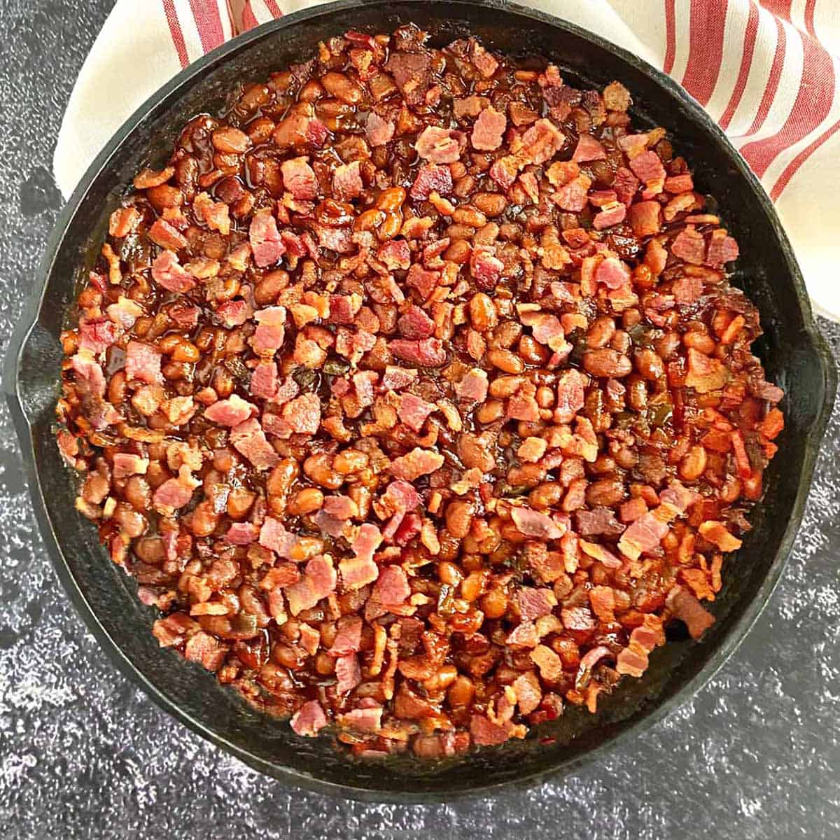 Smoked baked beans with bacon and brown sugar in a cast iron skillet.