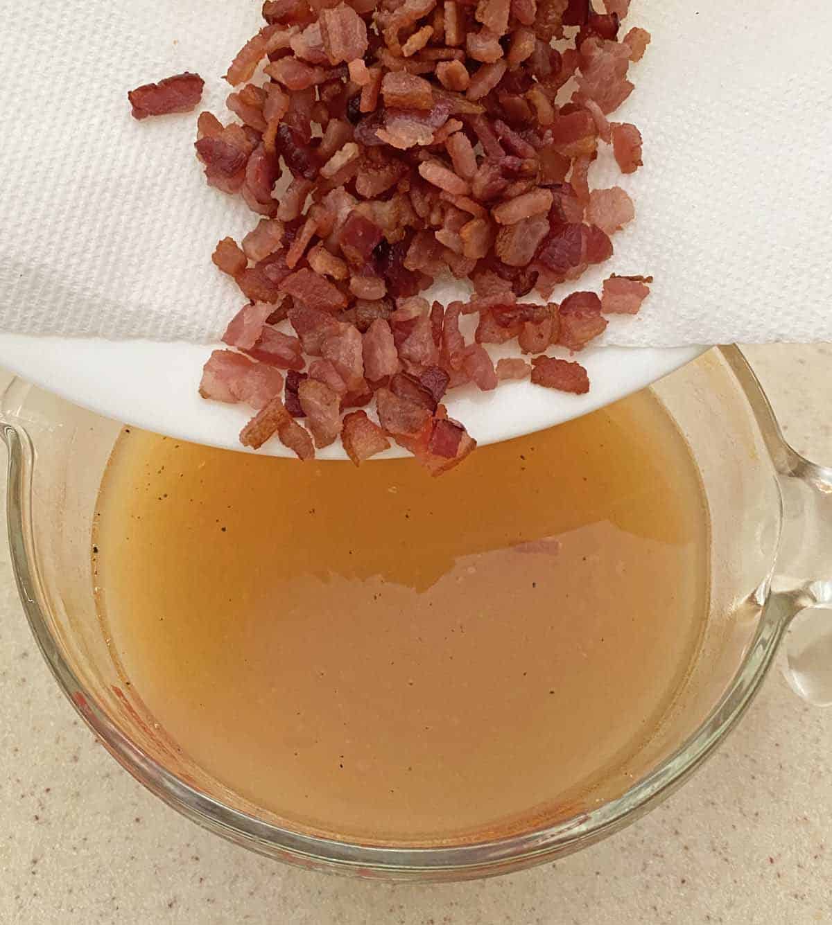 Adding cooked bacon to the stock in a glass measuring cup.