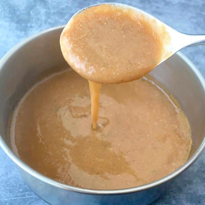 Bacon grease gravy in a saucepan, with a spoon lifting a drizzle of the gravy.