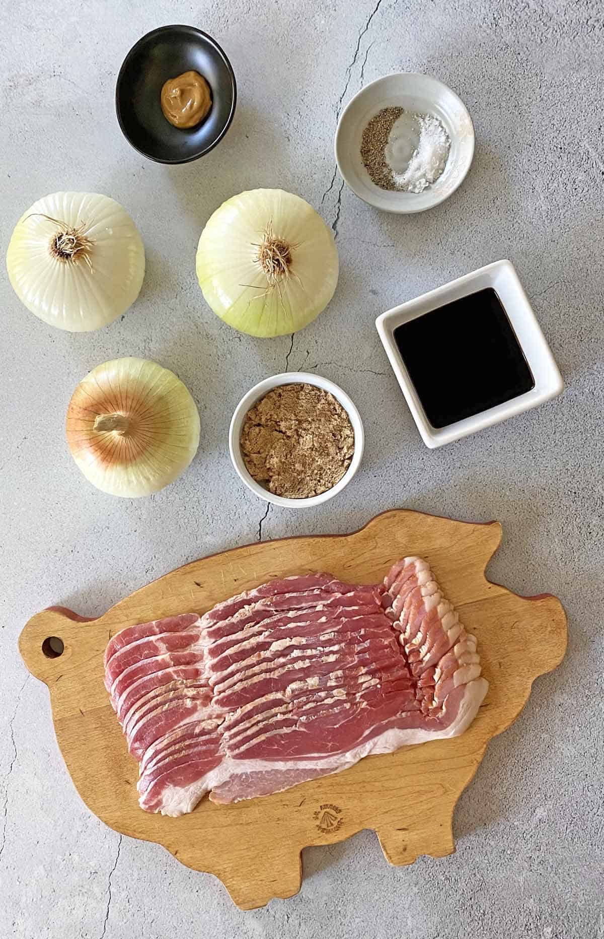 A dish with mustard, salt and pepper, 3 yellow onions, brown sugar, balsamic vinegar, and a pig-shaped cutting board with a pound of bacon.