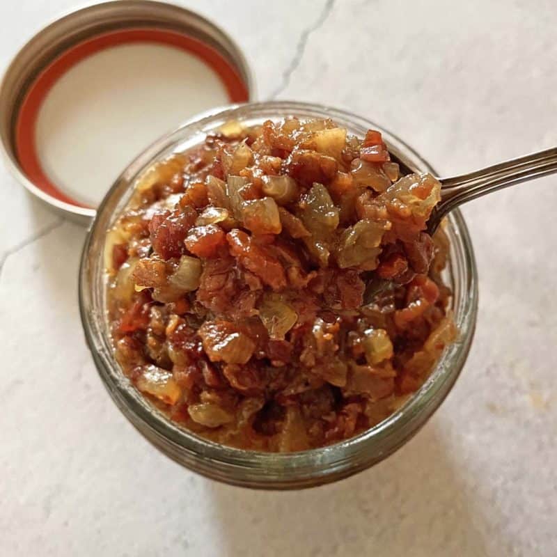 Bacon jam in a small mason jar with a spoon inside and the lid nearby.