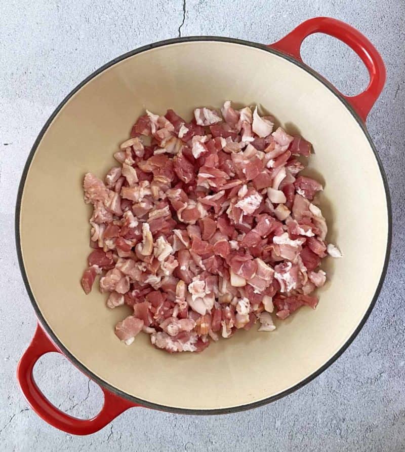Chopped uncooked bacon in a red Le Creuset pot, ready to be cooked.
