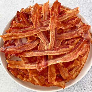 Two pounds of cooked bacon slices on a white platter.