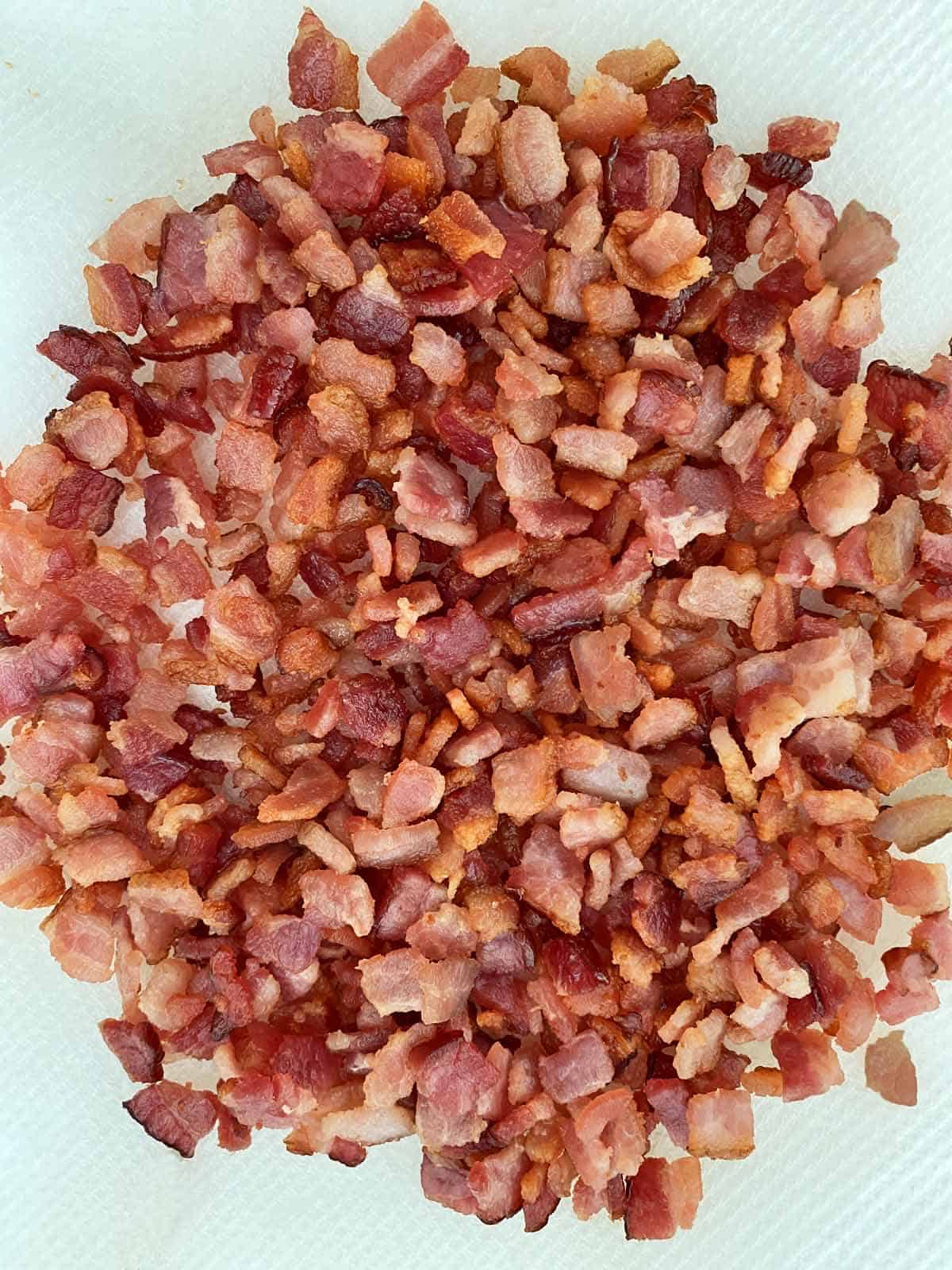 A pile of cooked, chopped golden brown bacon draining on paper towels.
