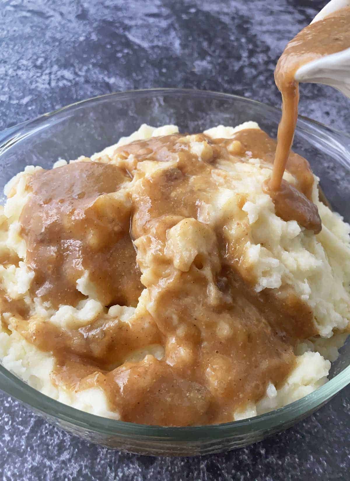 Drizzling a serving dish of mashed potatoes with bacon grease gravy from a gravy boat.