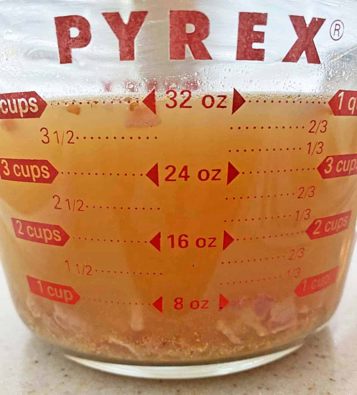 Cooked chopped bacon soaking in a glass Pyrex cup of hot stock to infuse it with flavor.