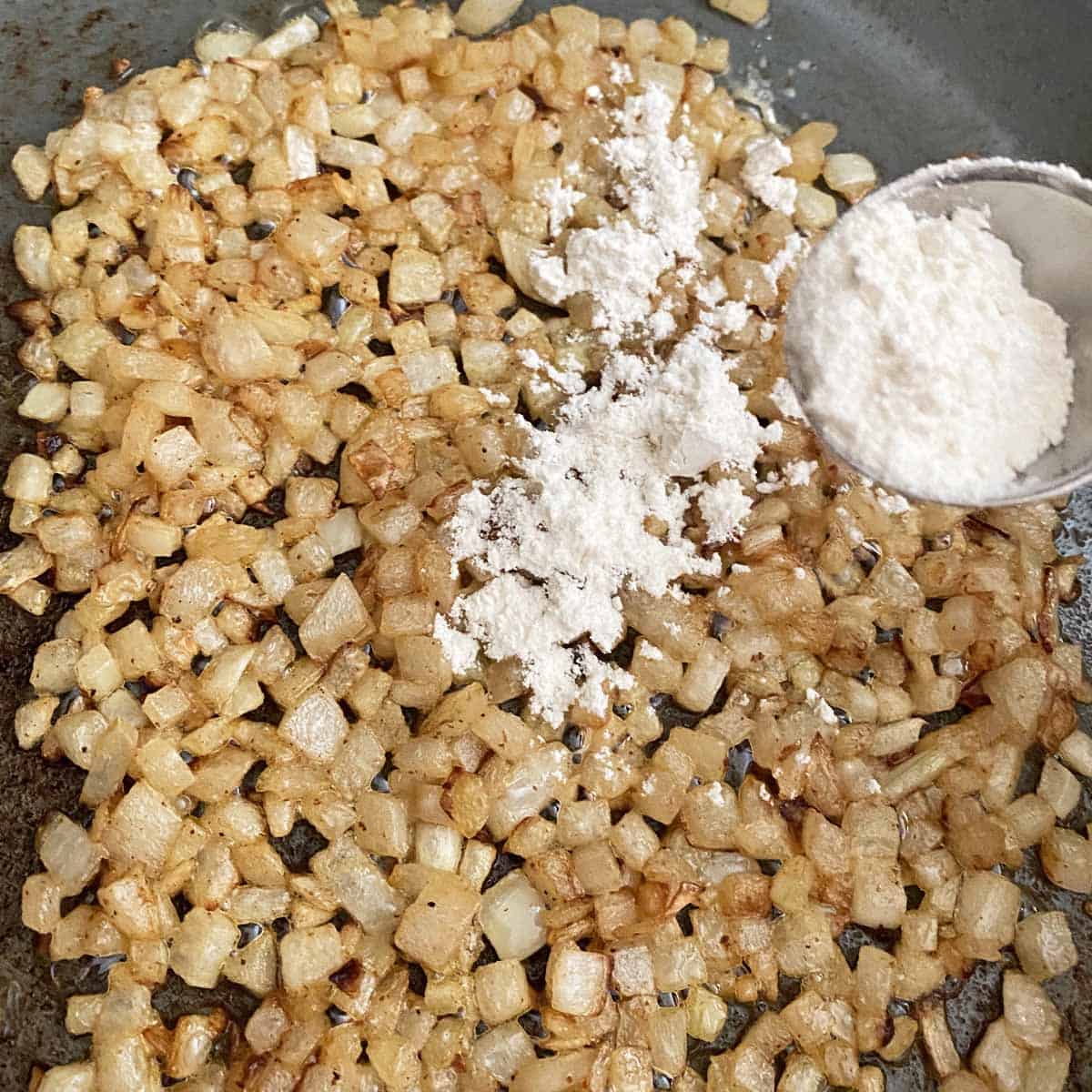 Sprinkling flour from a tablespoon onto the browned onions in a large skillet.