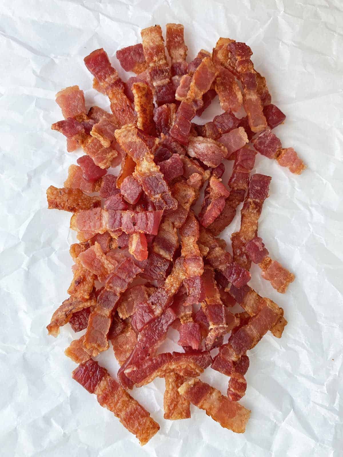 A pile of golden brown cooked bacon lardons on parchment paper.