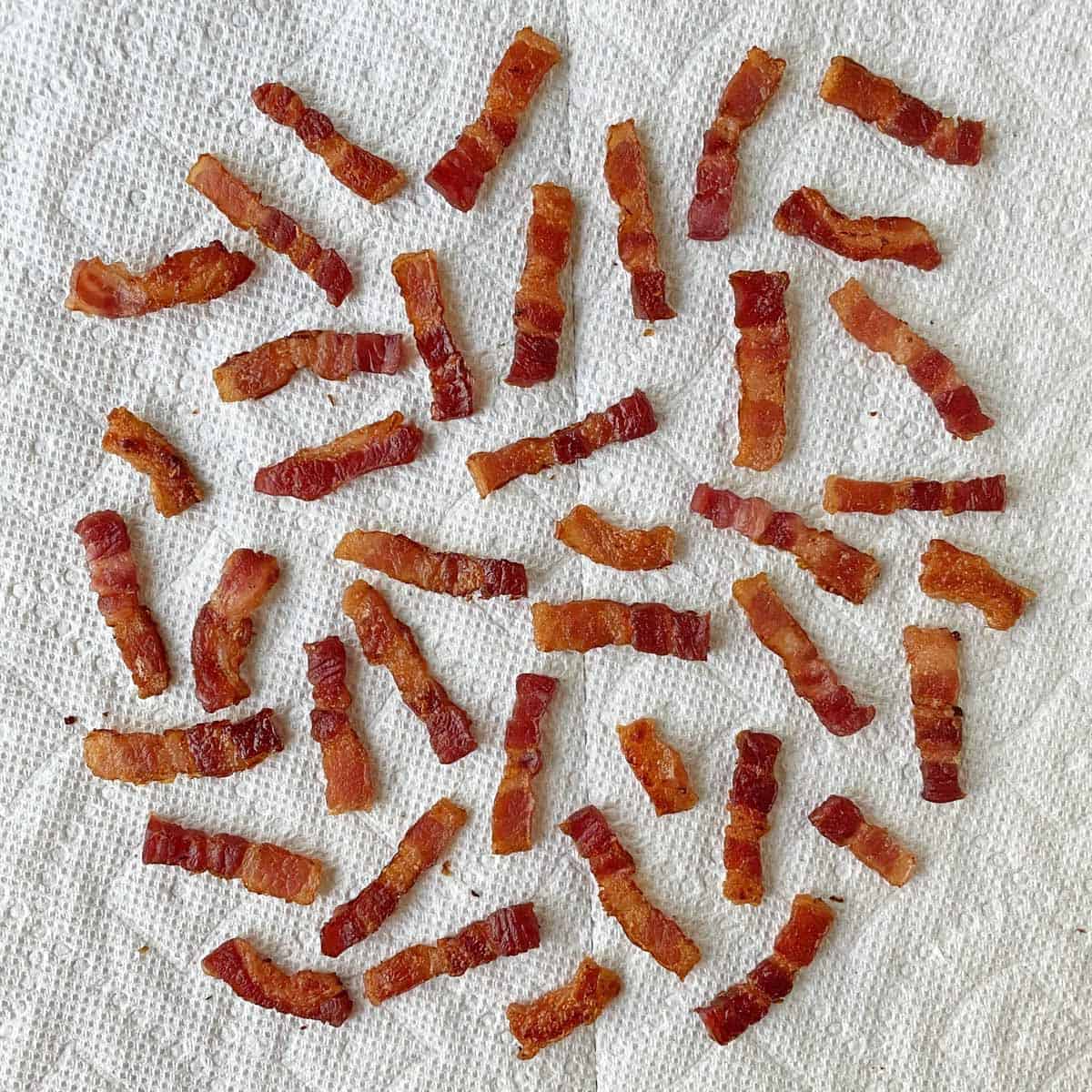Several dozen cooked bacon lardons draining on a paper towel.