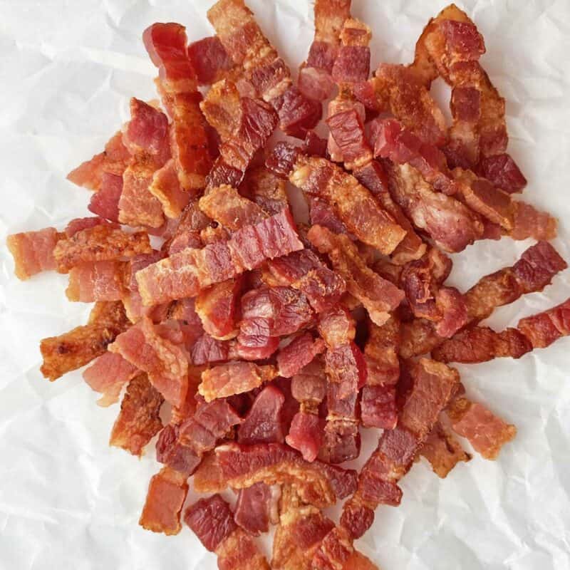 A pile of golden brown cooked bacon lardons on a piece of white parchment paper.