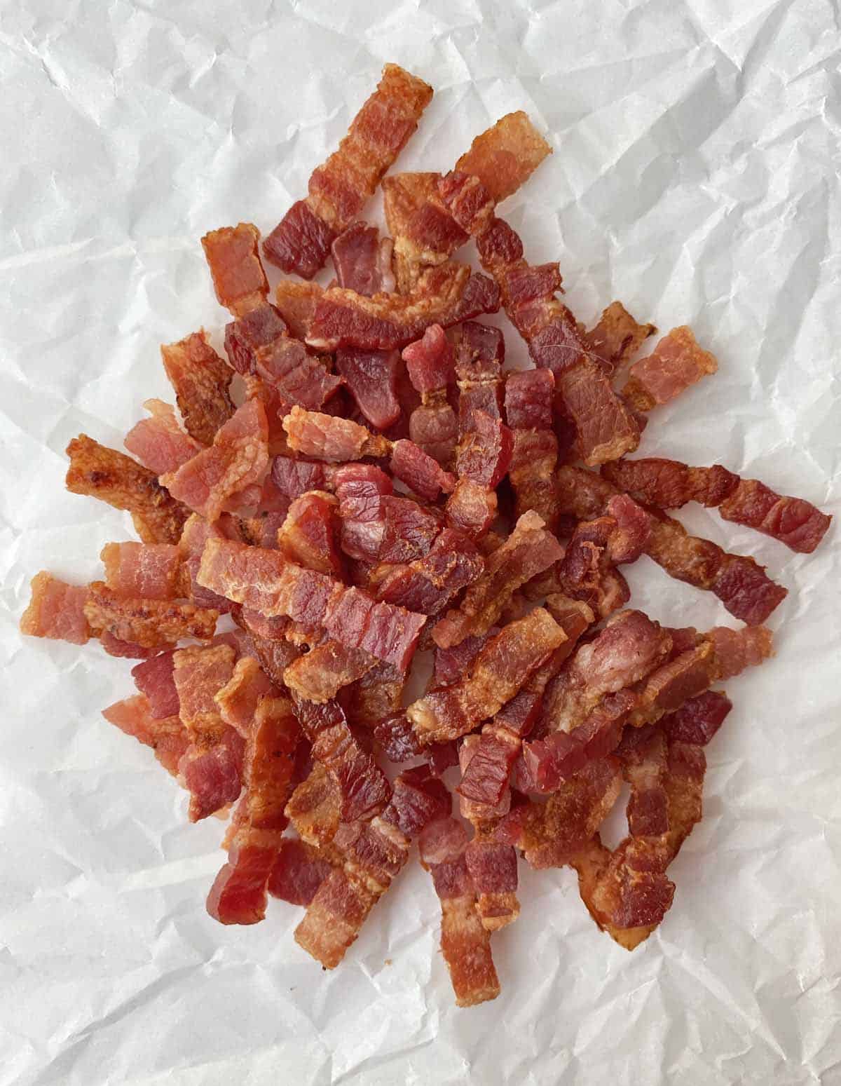 Finished bacon lardons piled on a crumpled piece of parchment paper.