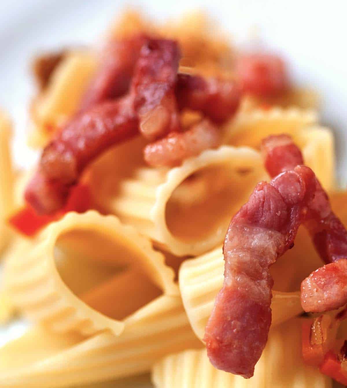 Penne pasta noodles with bacon lardons on top.