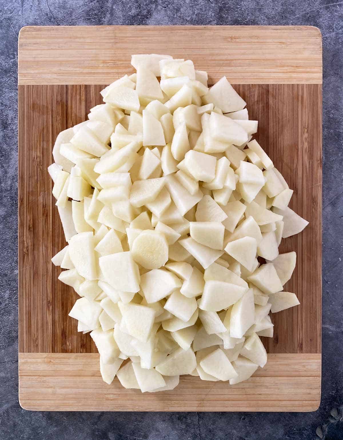 A pile of sliced, peeled potatoes on a bamboo cutting board.