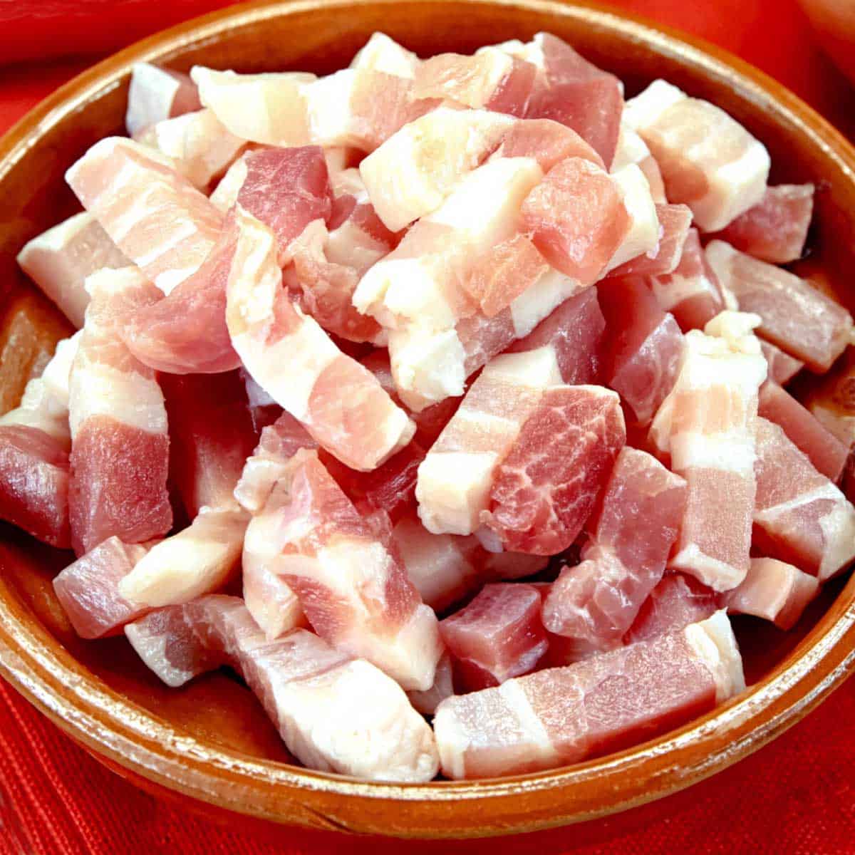 Raw bacon lardons cut from slab bacon in a red bowl.