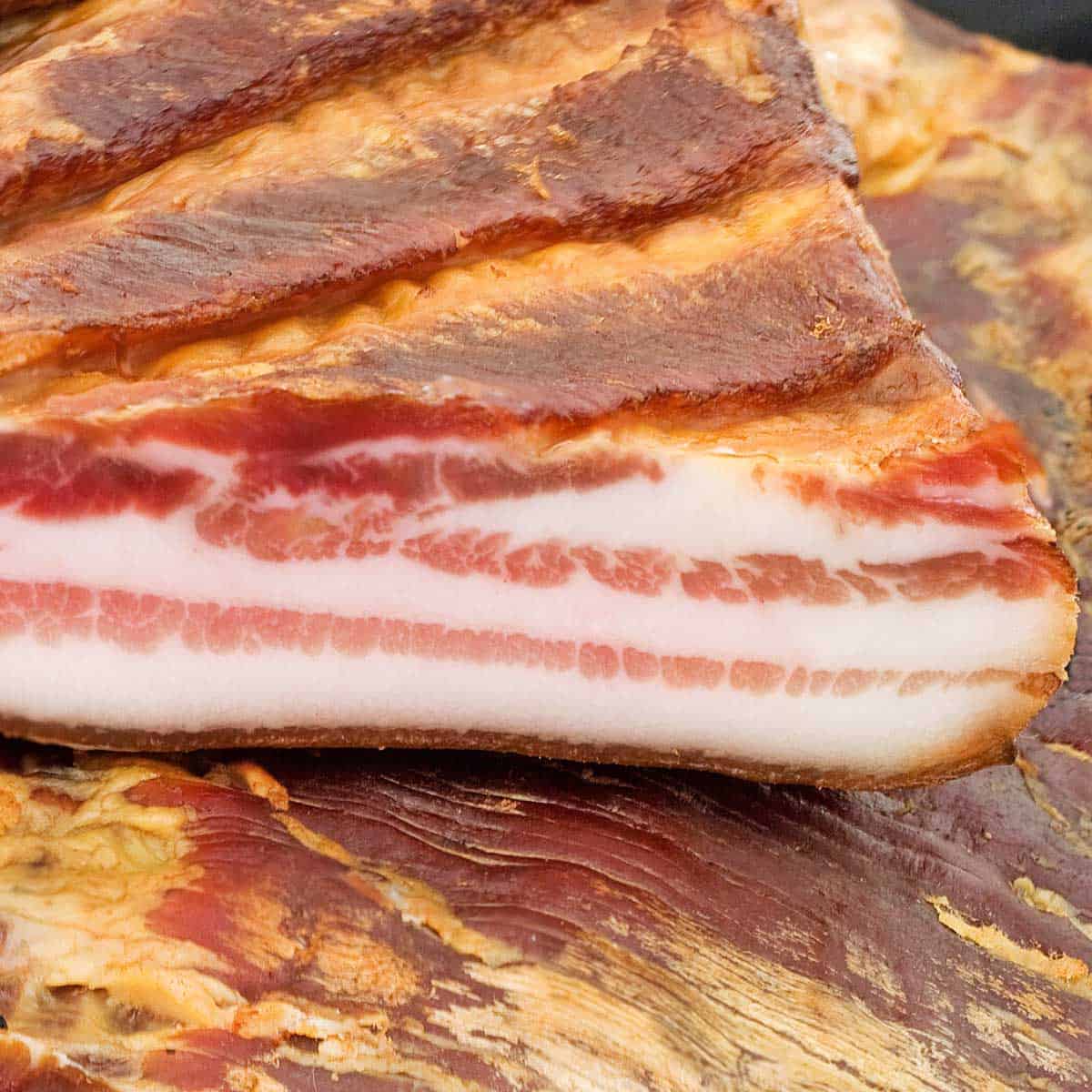 A cut slab of cured smoked bacon resting on top of an uncut bacon slab.
