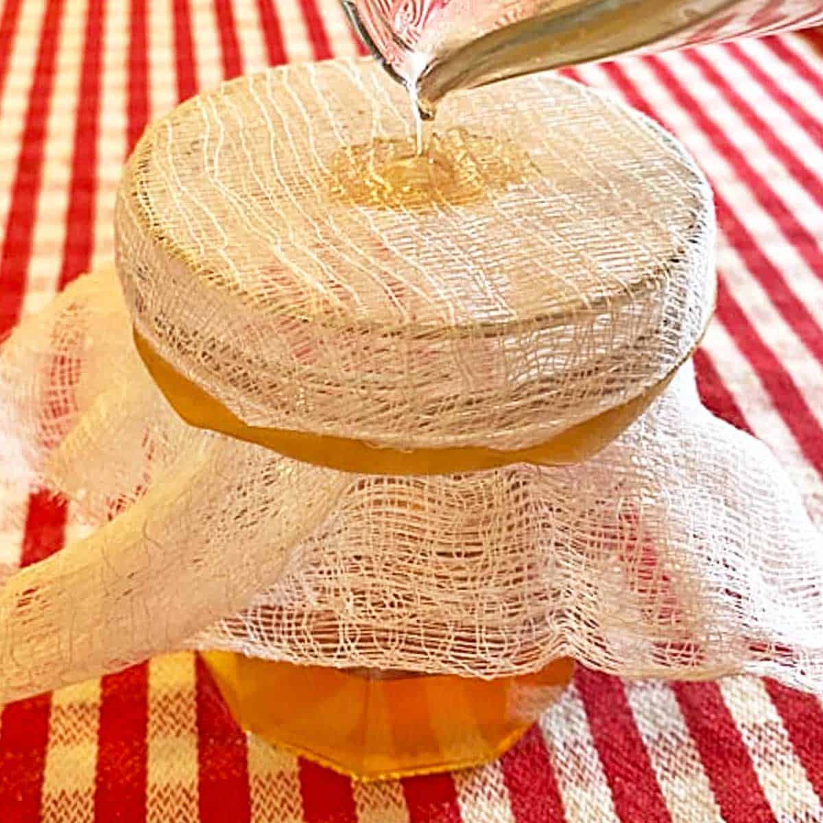 Pouring rendered bacon fat through a jar topped with cheesecloth held with a rubber band.