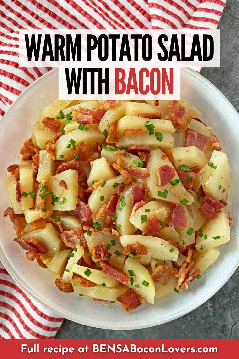 A serving bowl filled with warm bacon potato salad and garnished with chopped chives.