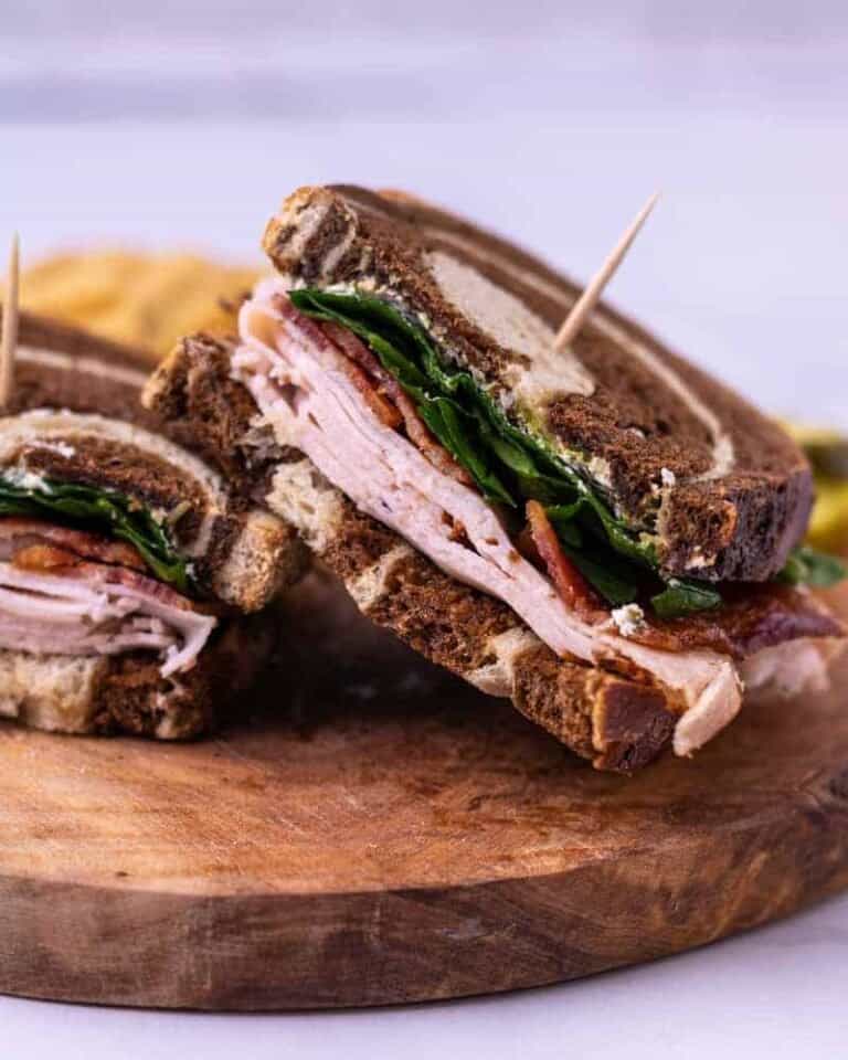A turkey sandwich with bacon and pesto, halved and held together with toothpicks.