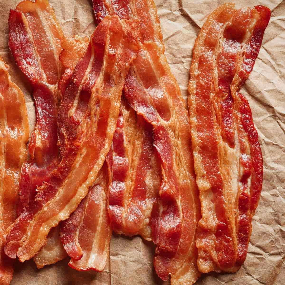 Eight slices of golden brown cooked bacon on a piece of brown paper.