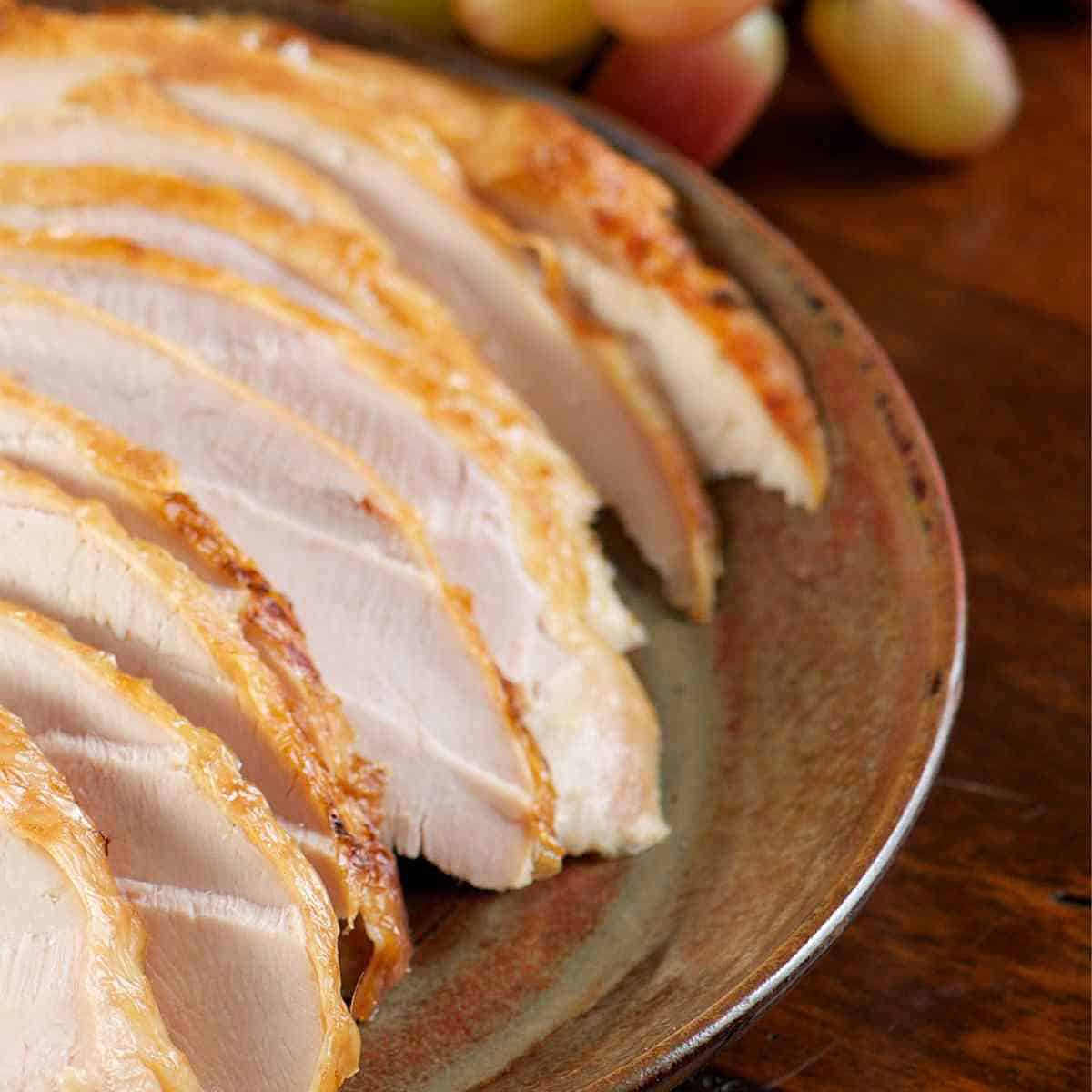 Sliced turkey on a ceramic platter, with grapes in the background.