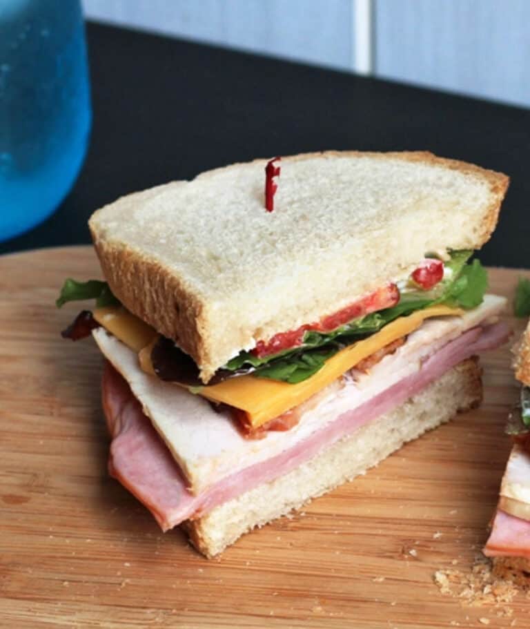 Club sandwich with sliced turkey, bacon, cheese, lettuce and tomato on a wood cutting board.