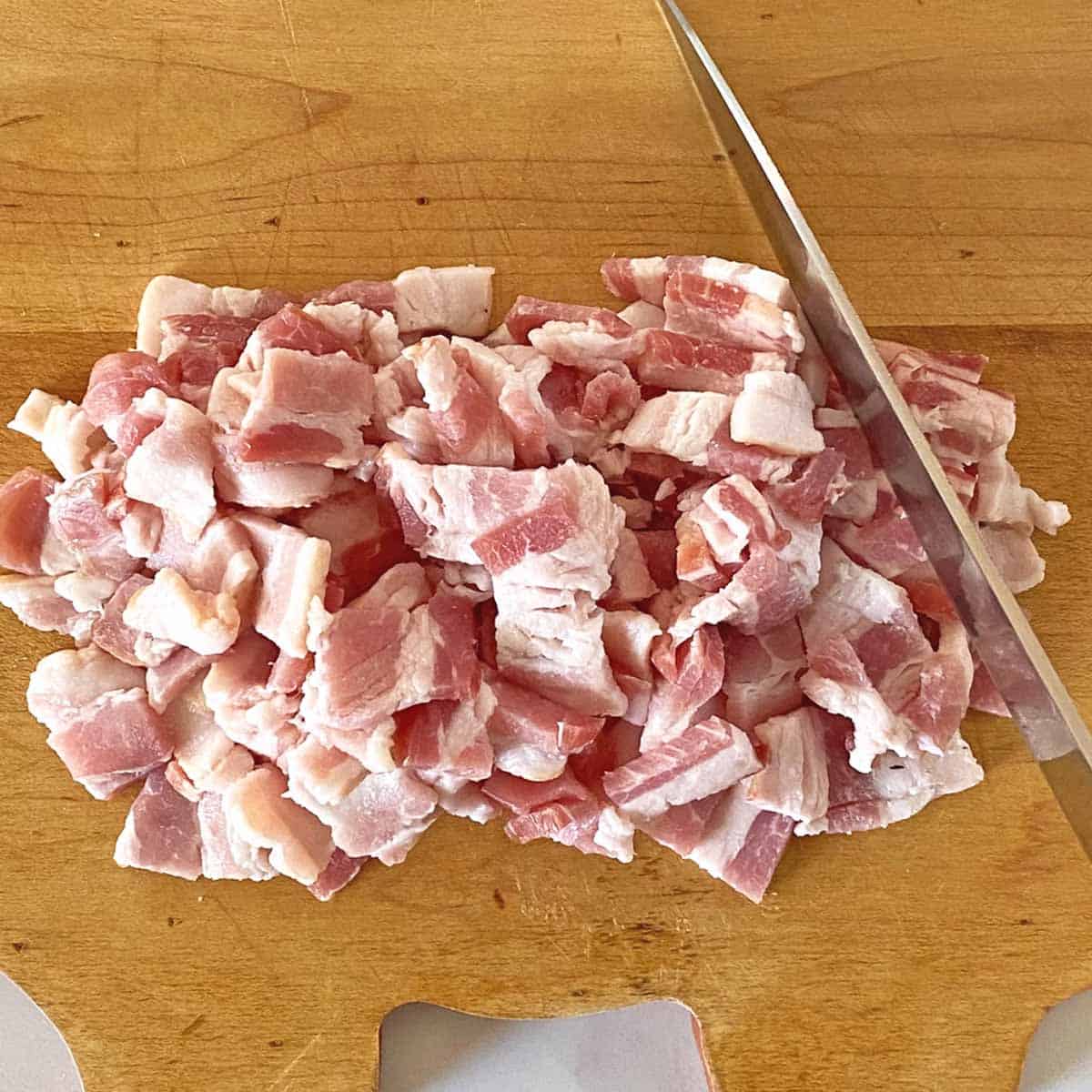A pile of chopped bacon and a knife on a cutting board.