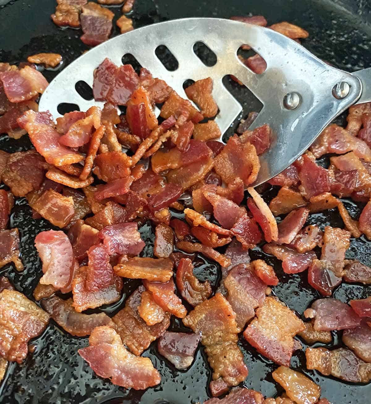 Cooking chopped bacon  in a skillet with a slotted spoon until golden brown.