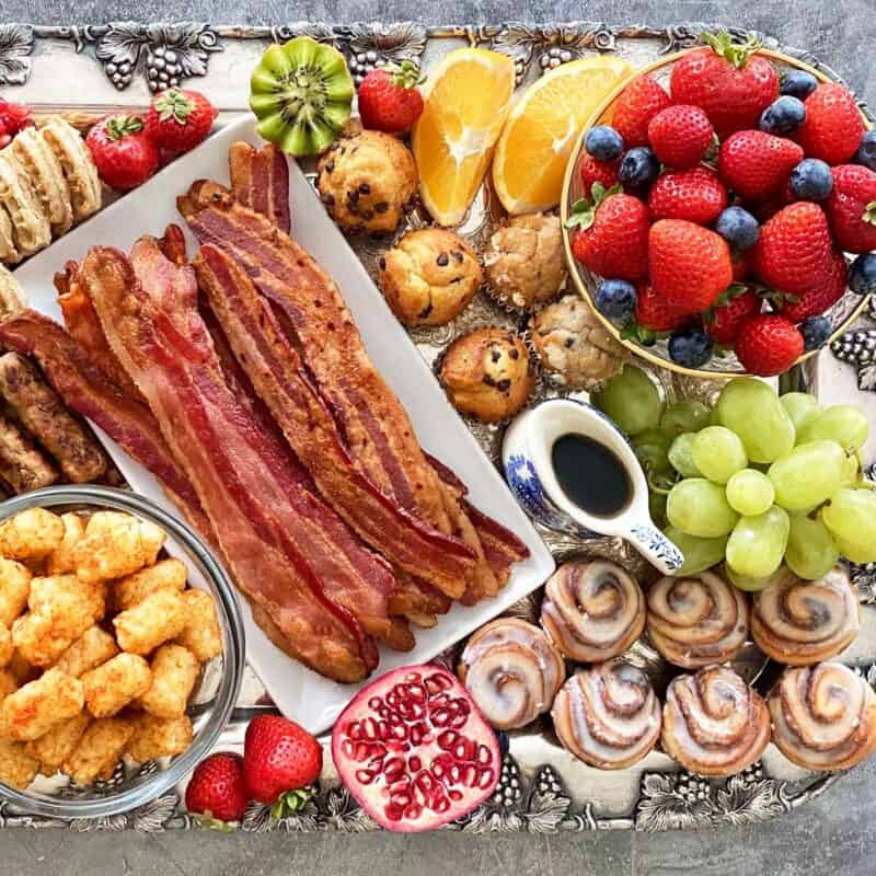 A breakfast charcuterie board loaded with bacon, fruit, sausage, potatoes, pastries and more.
