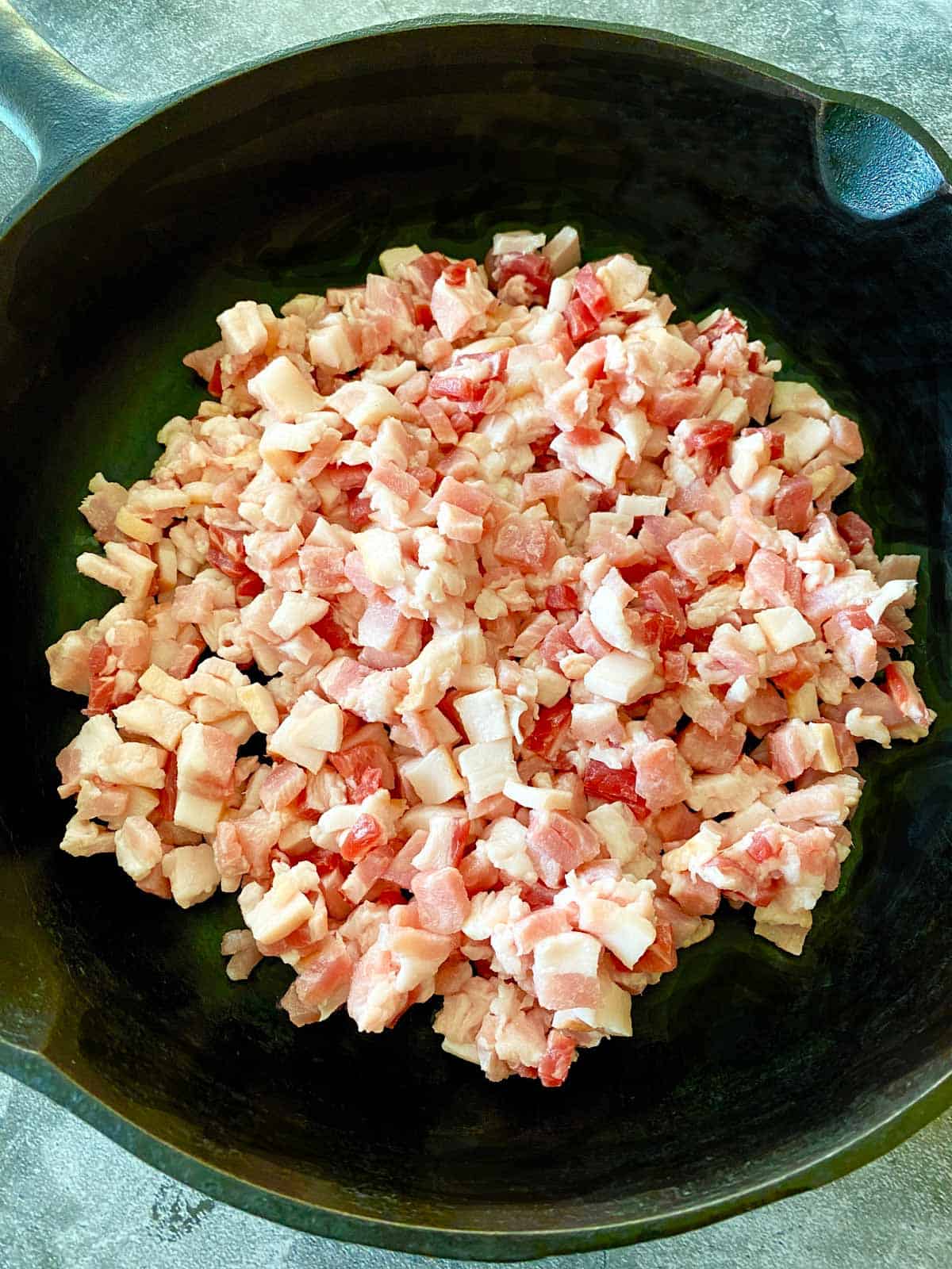 Finely chopped raw bacon in a cast iron skillet ready to be cooked.