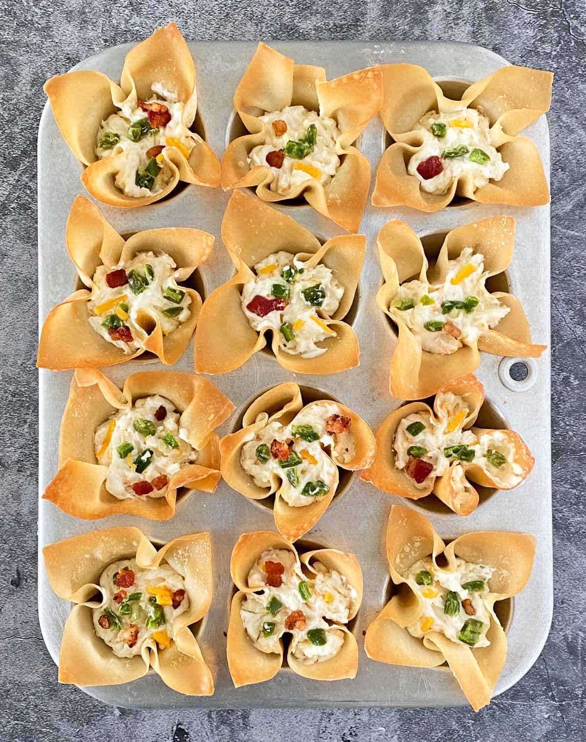 12 wonton cups in a muffin tin filled and ready for baking.