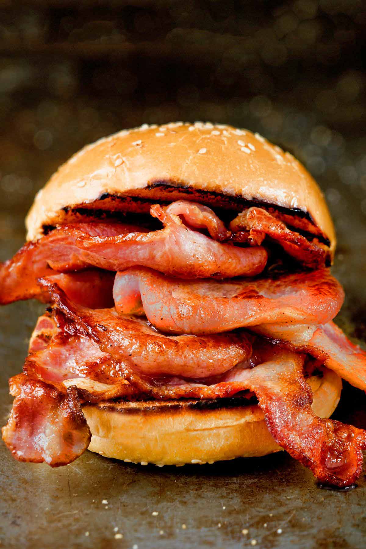 A fried back bacon sandwich on a sesame seed bun.