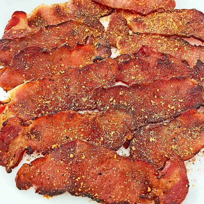 Cooked, seasoned British back bacon piled on a white plate.