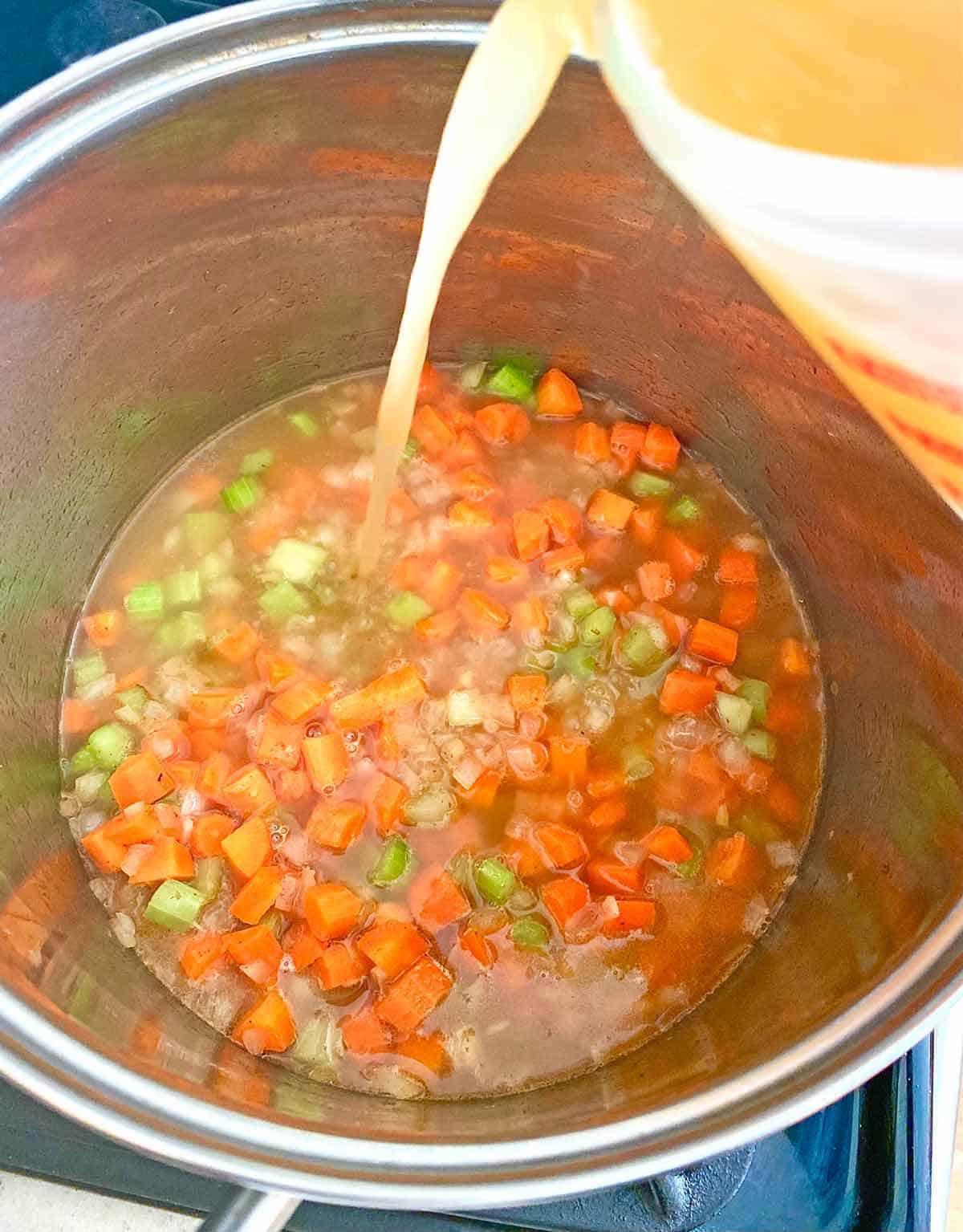 Pouring homemade chicken stock into the soup pot.