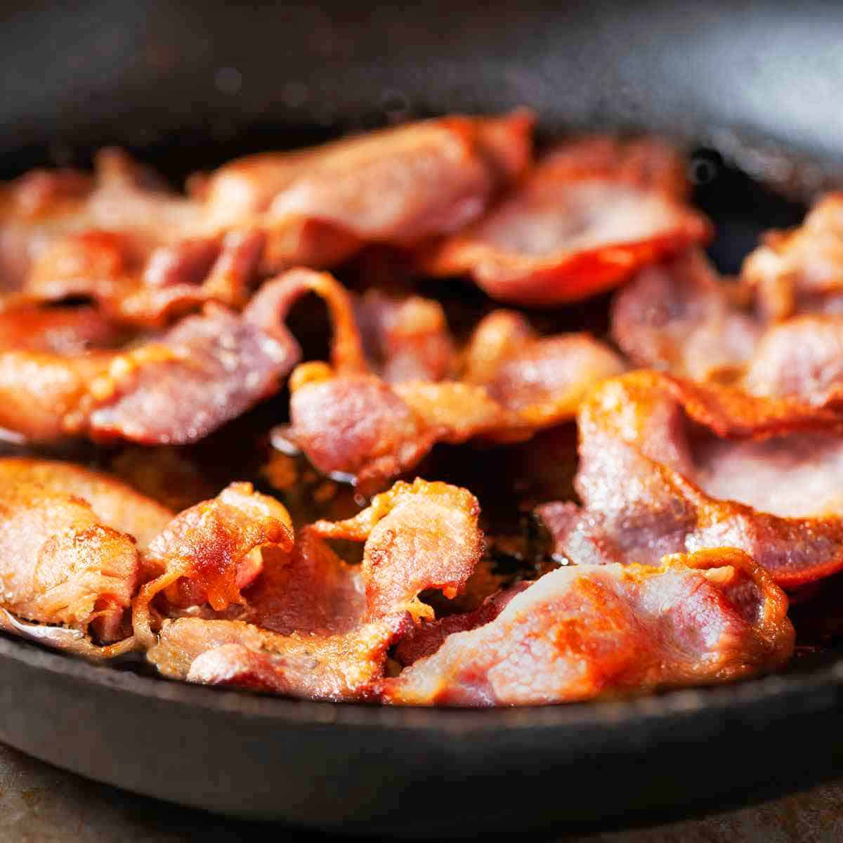 A pound of back bacon slices frying in a cast iron skillet.