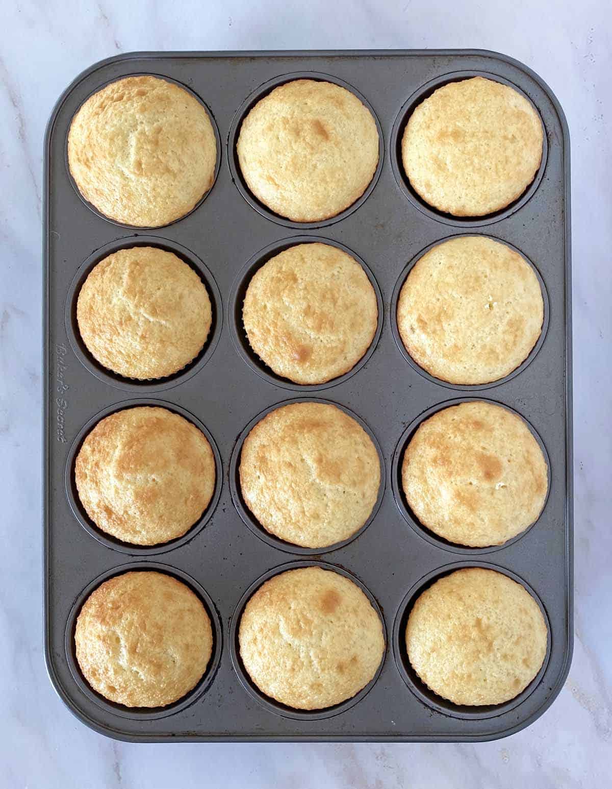 A dozen golden brown baked cupcakes in a cupcake pan.