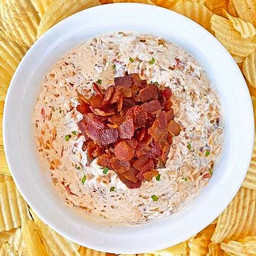 Cream cheese dip with bacon and onion in a white serving dish surrounded by potato chips.