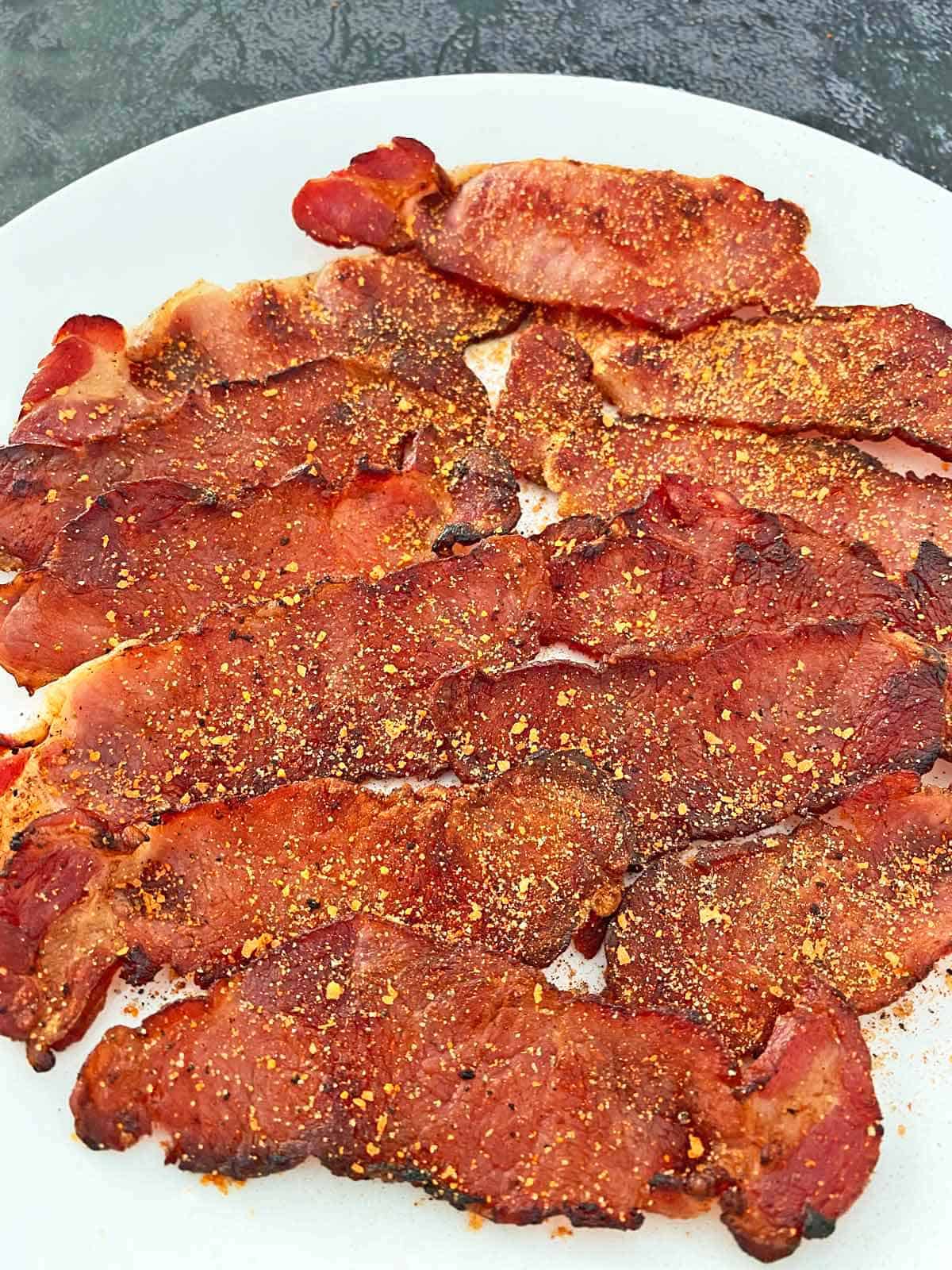 A dozen strips of cooked English back bacon on a white plate.