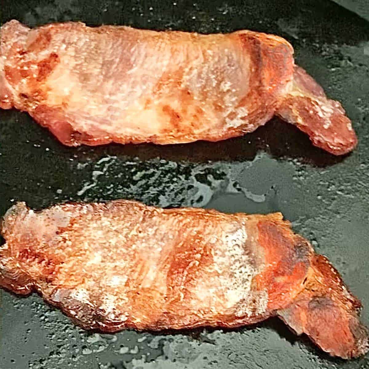 Two strips of browned back bacon in a skillet.