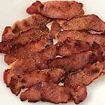 15 slices of pan fried back bacon sprinkled with seasonings on a white plate.