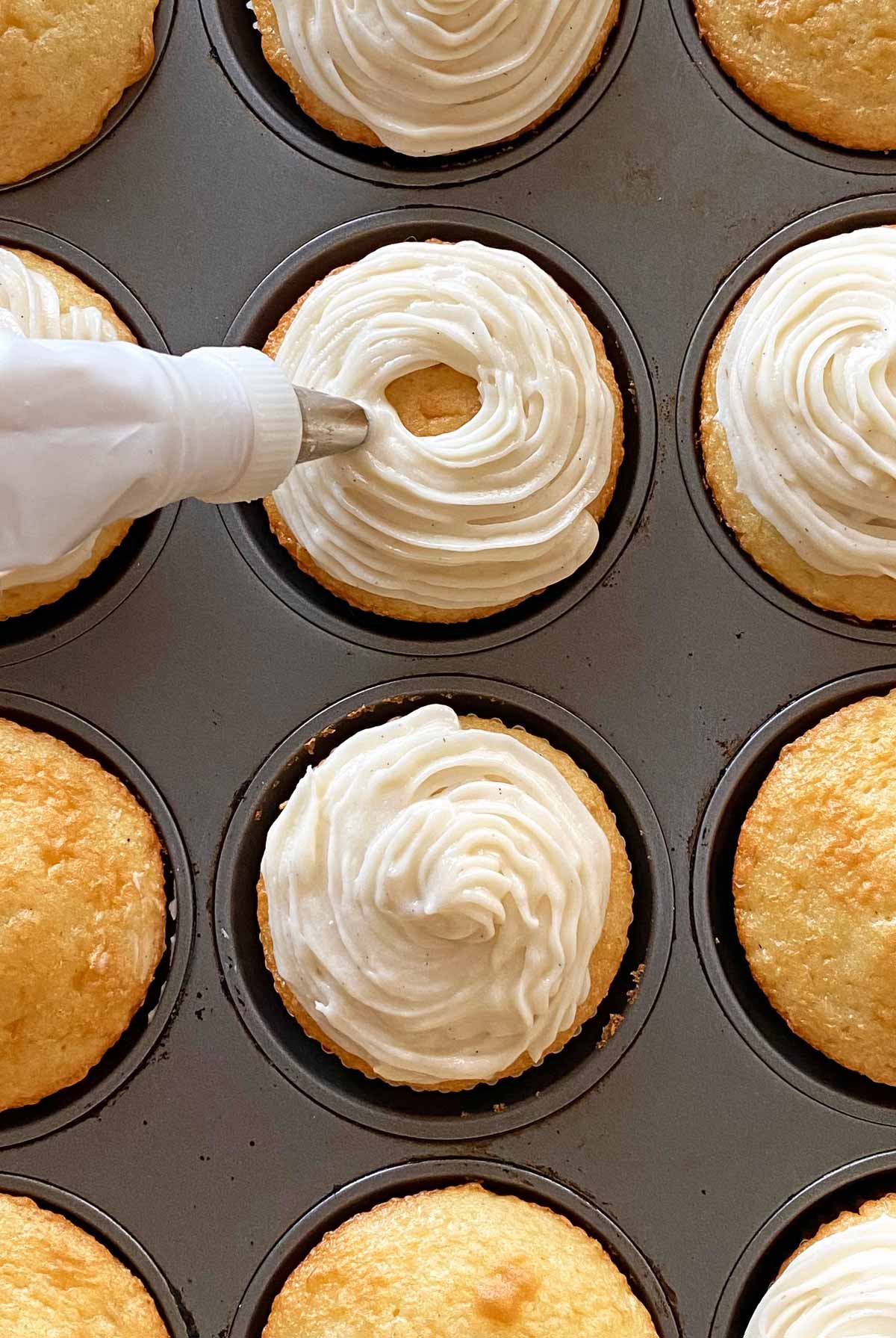 Piping frosting on a cupcake using a pastry bag.