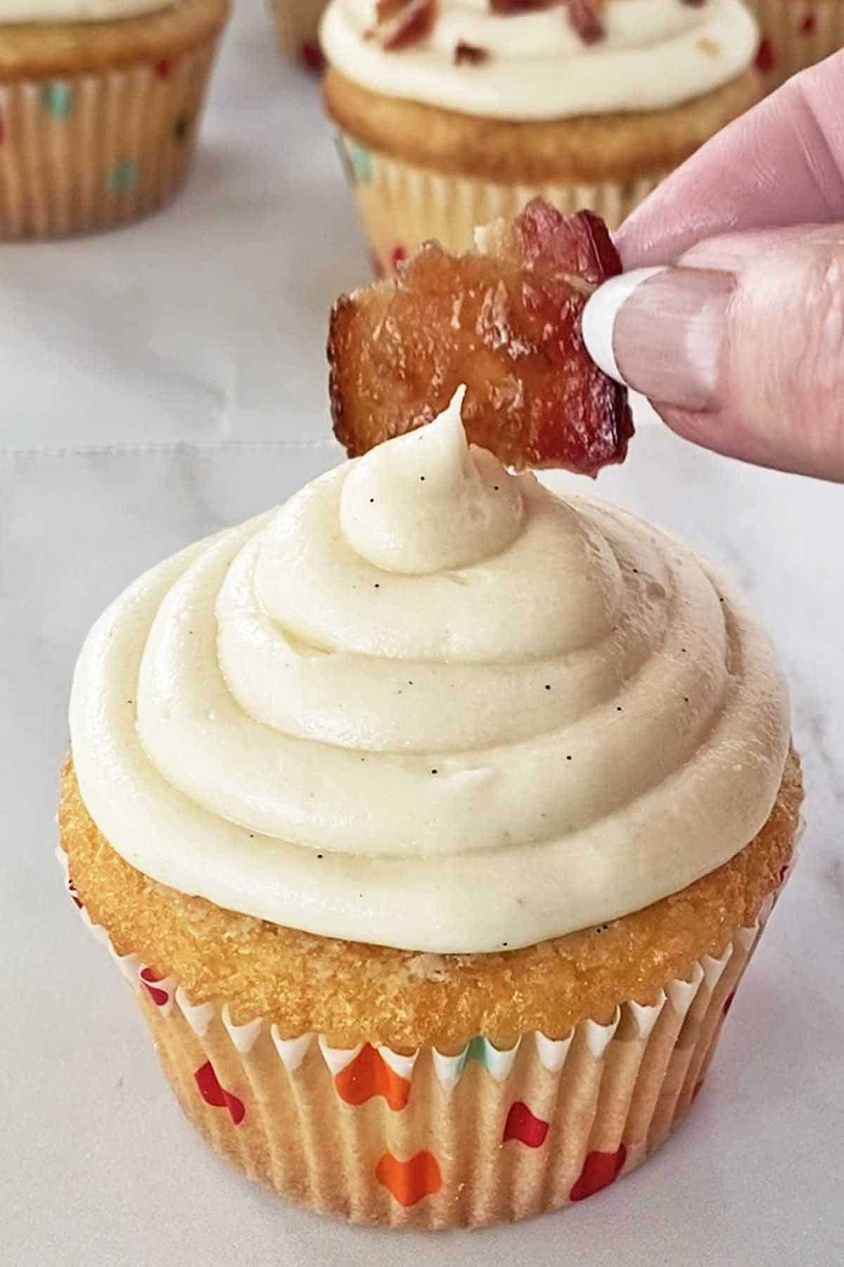 Garnishing a frosted maple bacon cupcake with a piece of maple candied bacon.