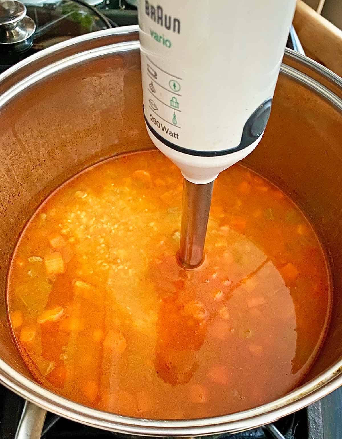 Blending some of the soup mixture with an immersion blender in a stock pot.