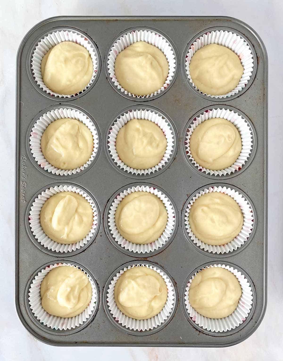 A cupcake pan with 12 paper liners filled with cupcake batter.