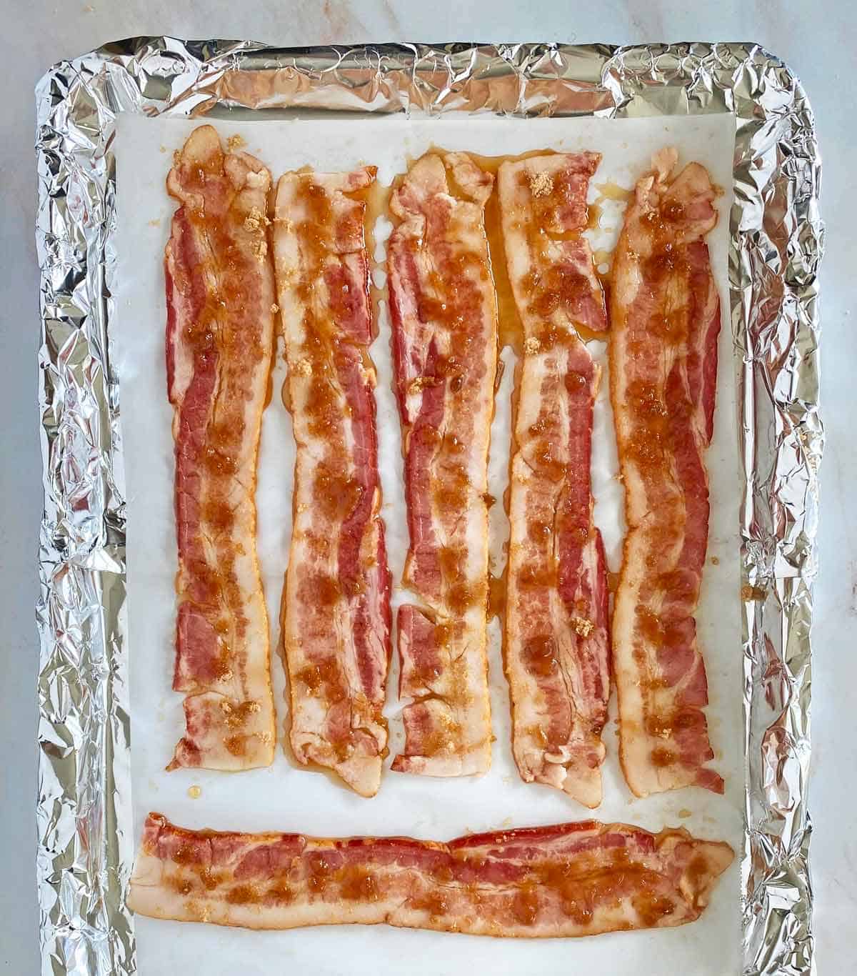 6 strips of uncooked bacon coated with maple syrup and brown sugar on a foil lined baking sheet.